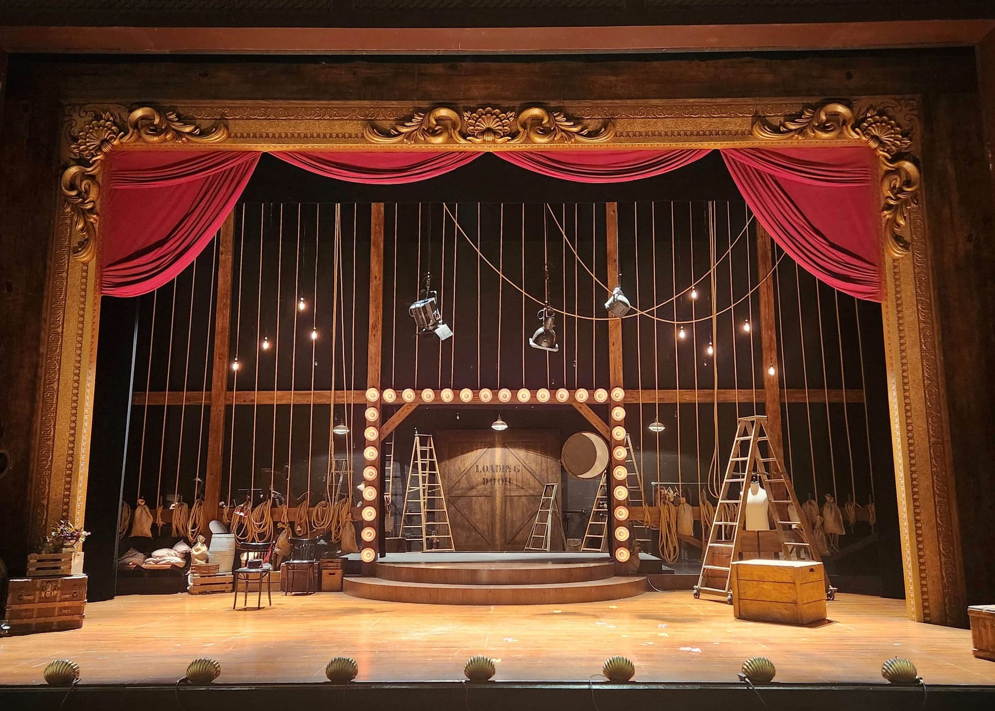 A stage set shows hanging spotlights, a ladder, and bulb lights.