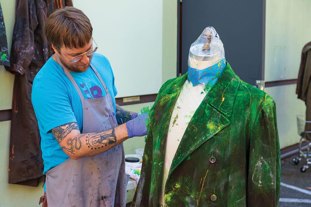 A craftsman works on a green-painted jacket in the scene shop.