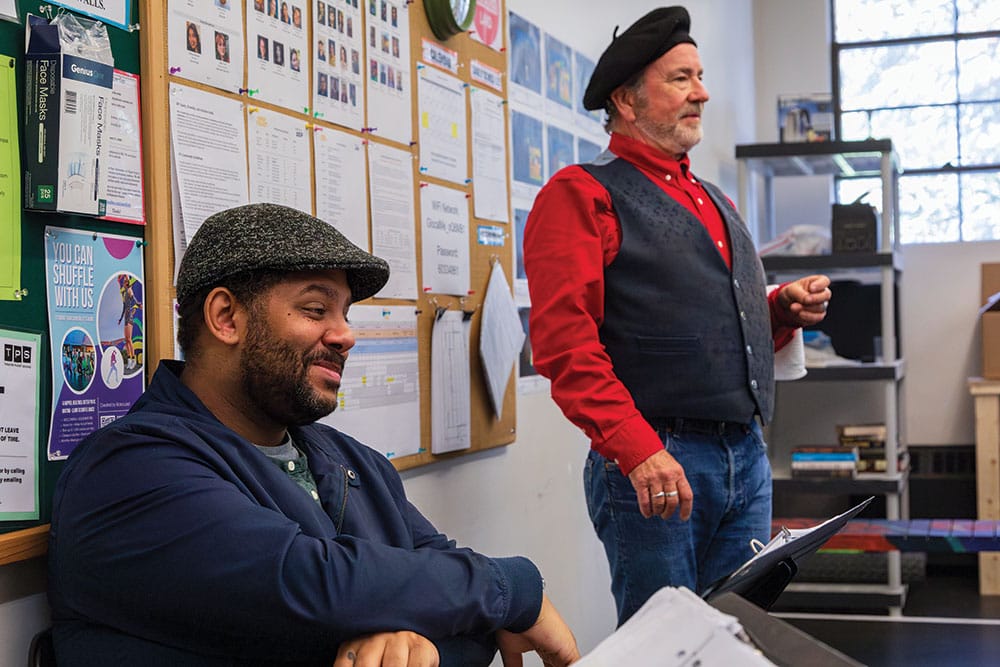 Andrew Lee Creech, seated in a blue jacket, and Rob Burgess, standing in a red shirt and gray vest, in rehearsal for Primary Trust