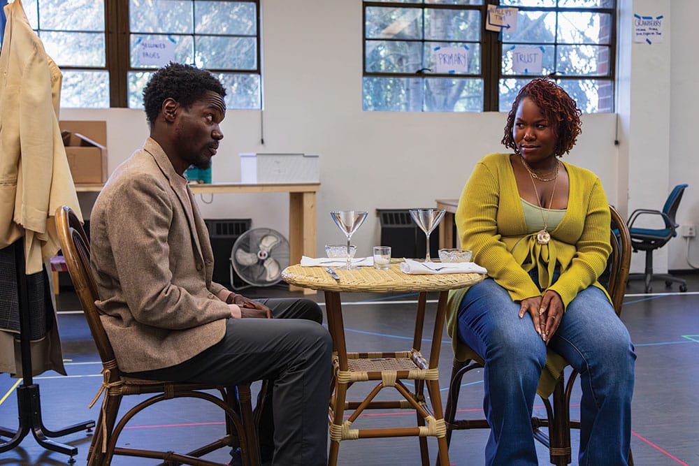 Stephen Tyrone Williams and Allyson Lee Brown in rehearsal for Primary Trust, seated at a small table set for dinner.