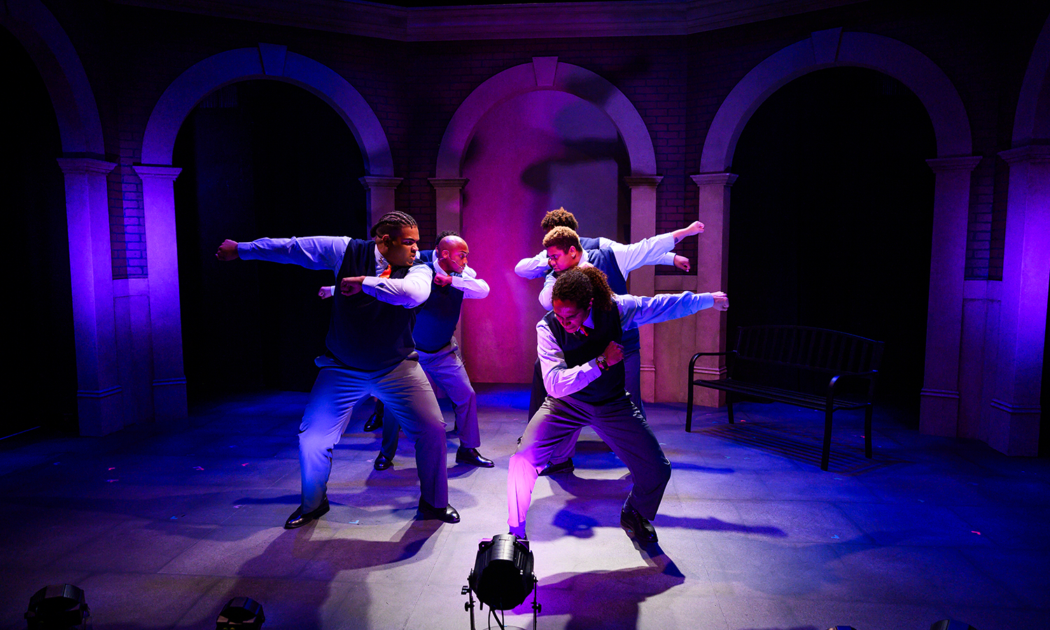 A group of young men wear school uniforms and have their arms up in dance,