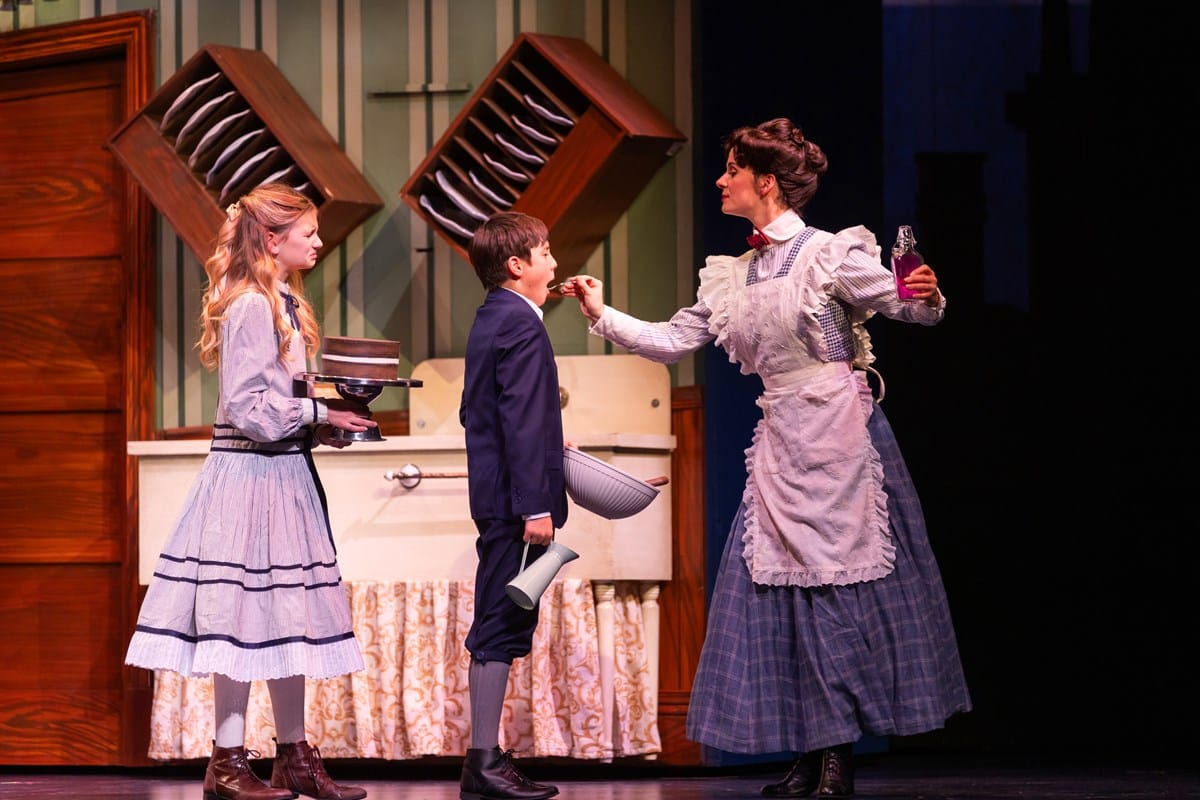 A woman spoons medicine into a boy's mouth. A girl looks on with a disgusted look.