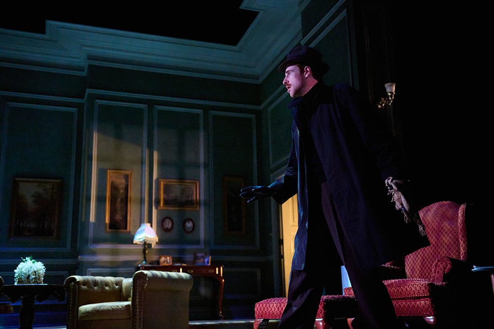 A man dressed all in black sneaks through a study in a home.