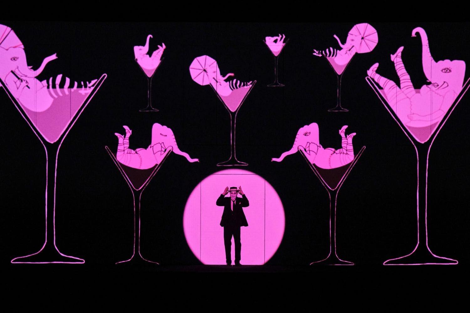 A man stands in a purple spotlight with elephants in martini glasses.