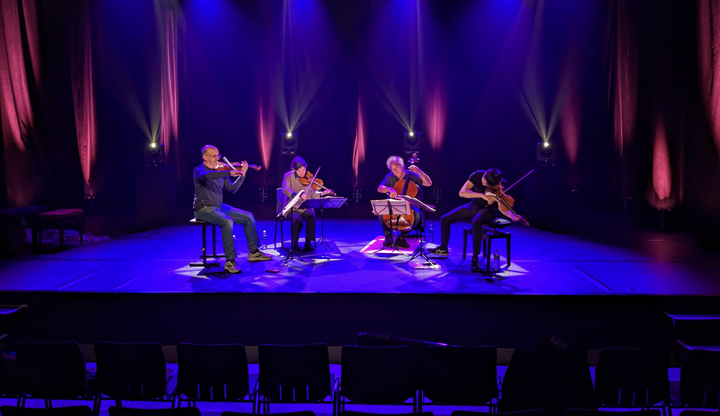 The Takács Quartet performs on a stage with blue lighting on them.