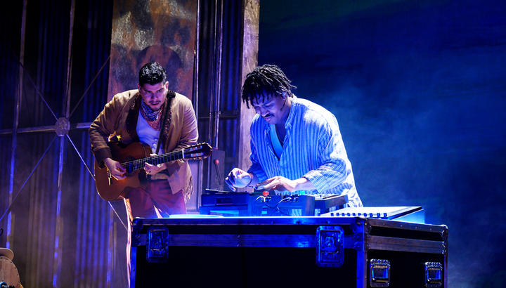 Two musicians are on stage, one plays the guitar while the other is at a turntable.