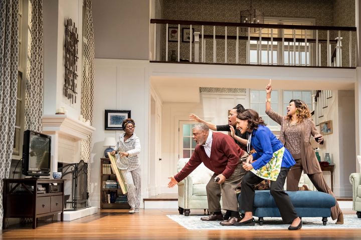 A stage shows a living room with a group of people running towards the tv in a panic.