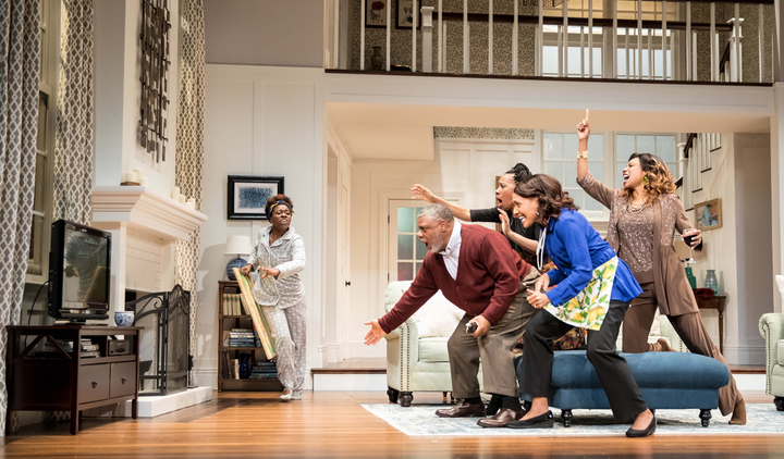 A stage shows a living room with a group of people running towards the tv in a panic.