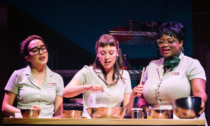 Three women wearing waitress uniforms are baking together.