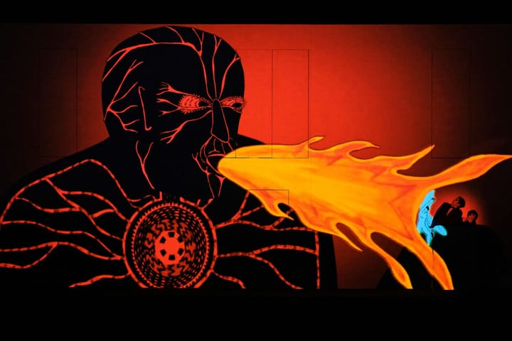 A giant background graphic image of a man blowing fire at two men on stage.