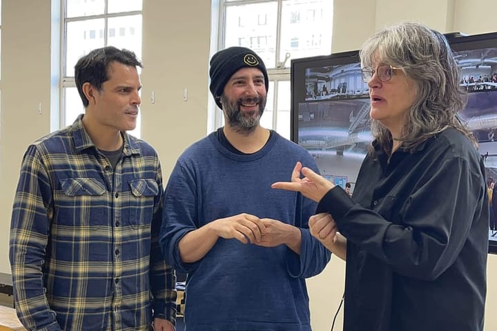 Two men and a woman talk to each other in rehearsal.